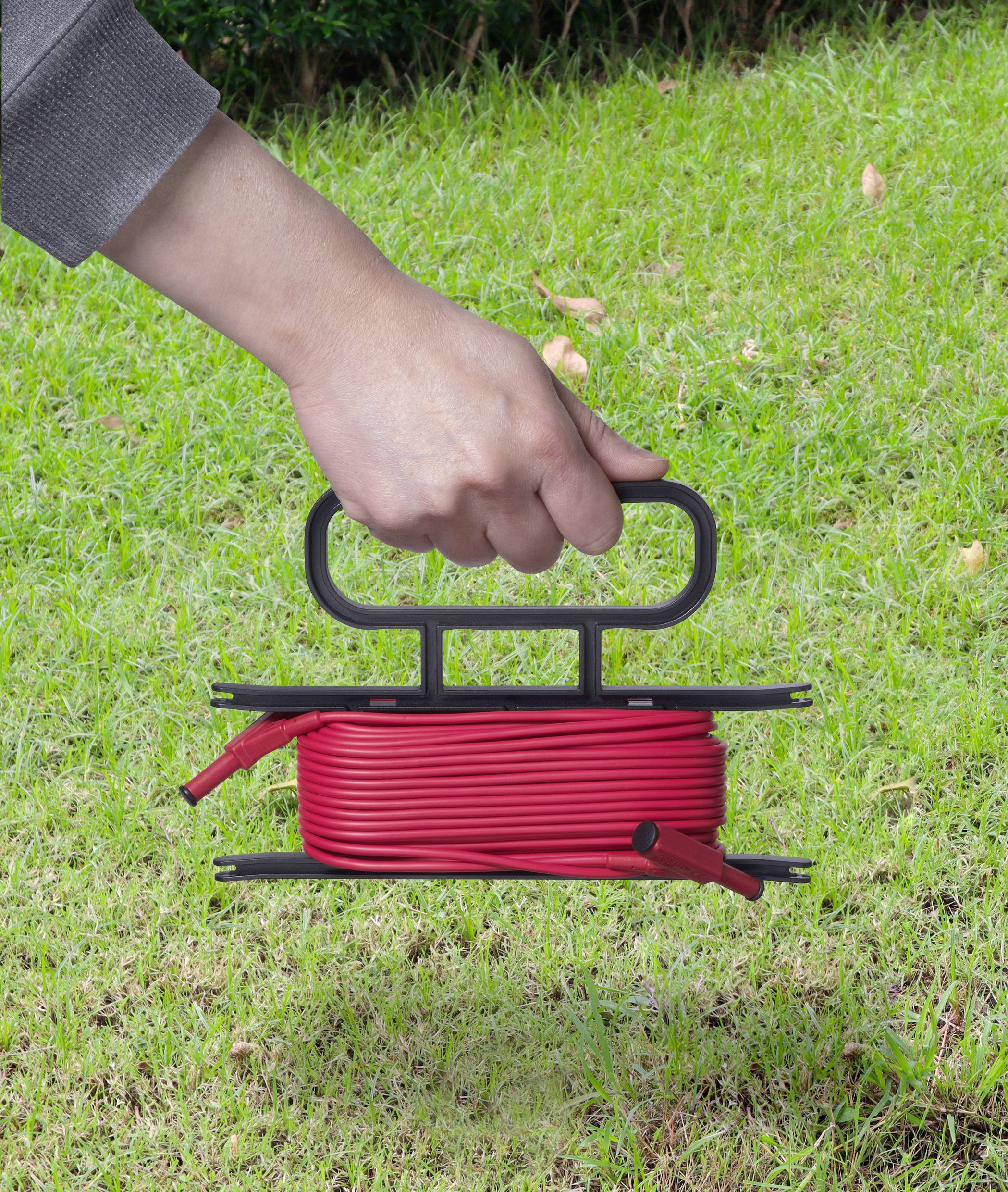 Person hält eine rote, aufgerollte Kabeltrommel mit Griff über grünem Rasen.