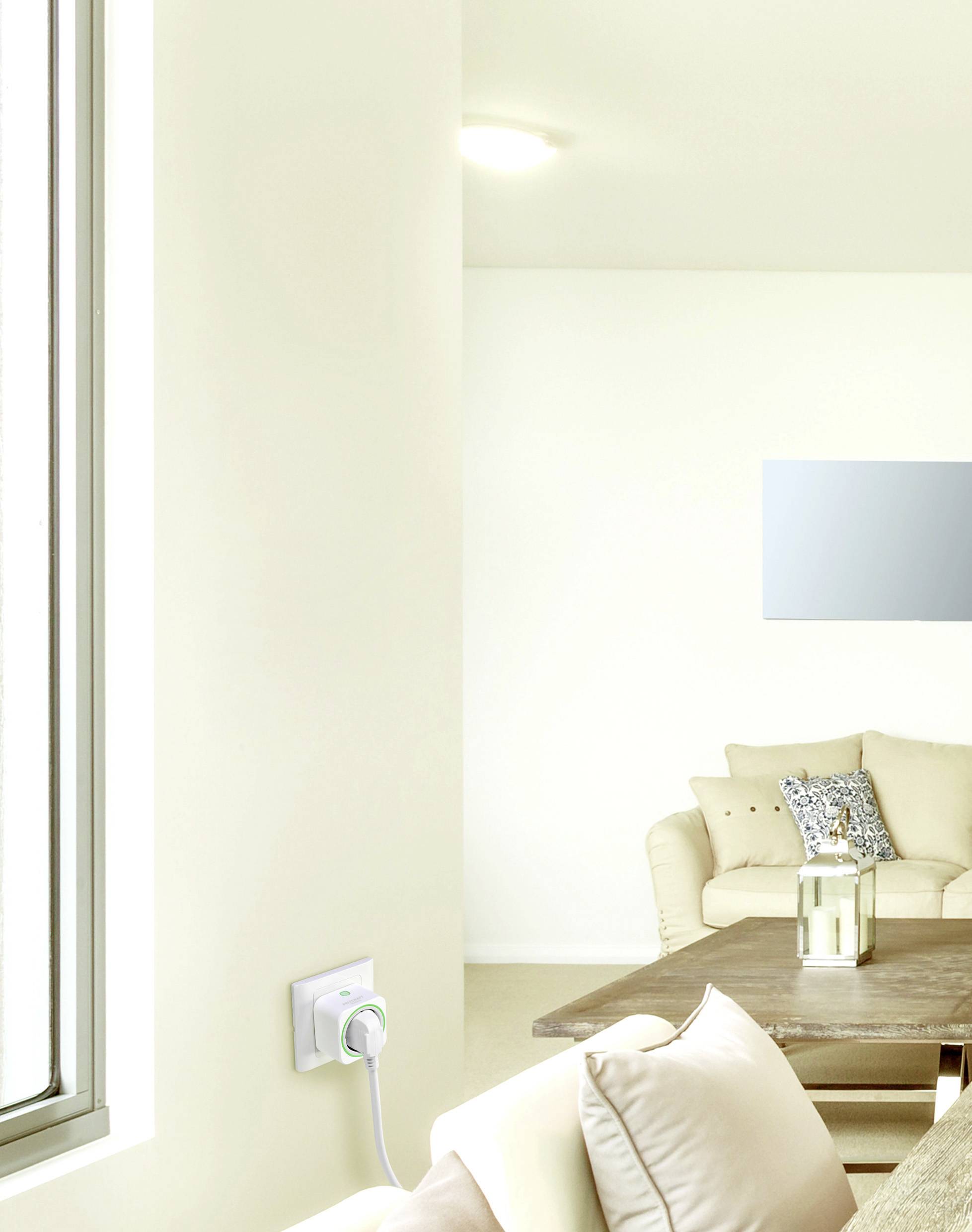 Wohnzimmer mit hellem Sofa und Holztisch, moderne Leuchte an der Decke. Ein intelligenter Stecker ist an der Wand installiert.