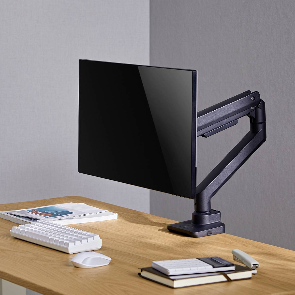 Ein sauberer Schreibtisch mit einem Computermonitor auf einem verstellbaren Arm, Tastatur und zwei Bücher; moderne, minimalistische Umgebung.