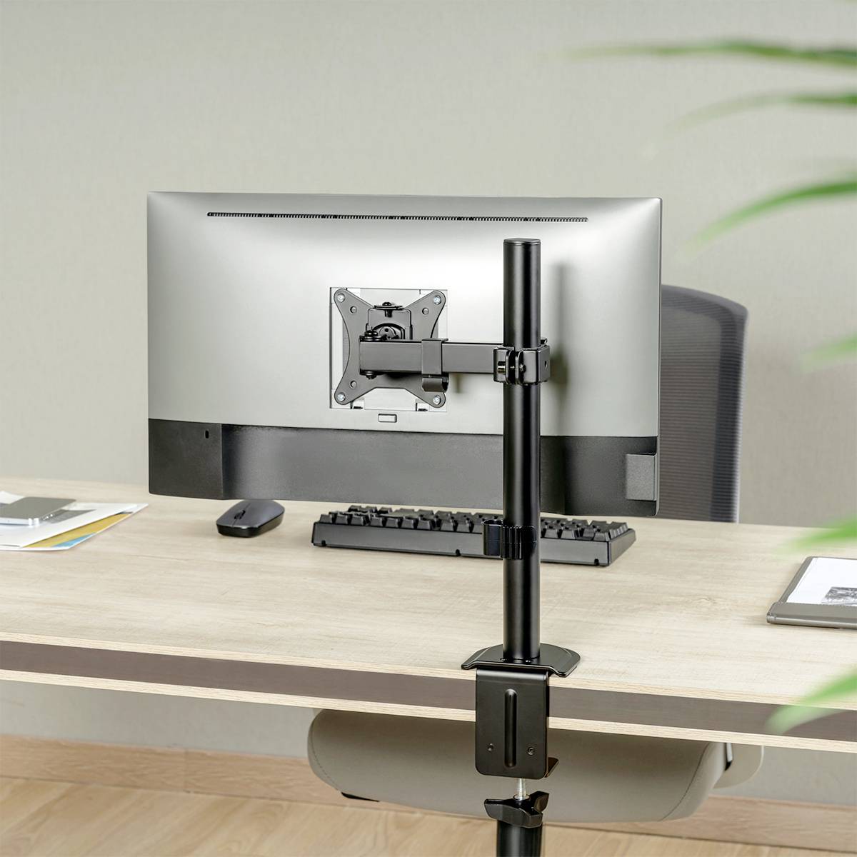 Ein Computermonitor ist rückseitig an einer höhenverstellbaren Halterung befestigt. Der Schreibtisch ist aus hellem Holz.