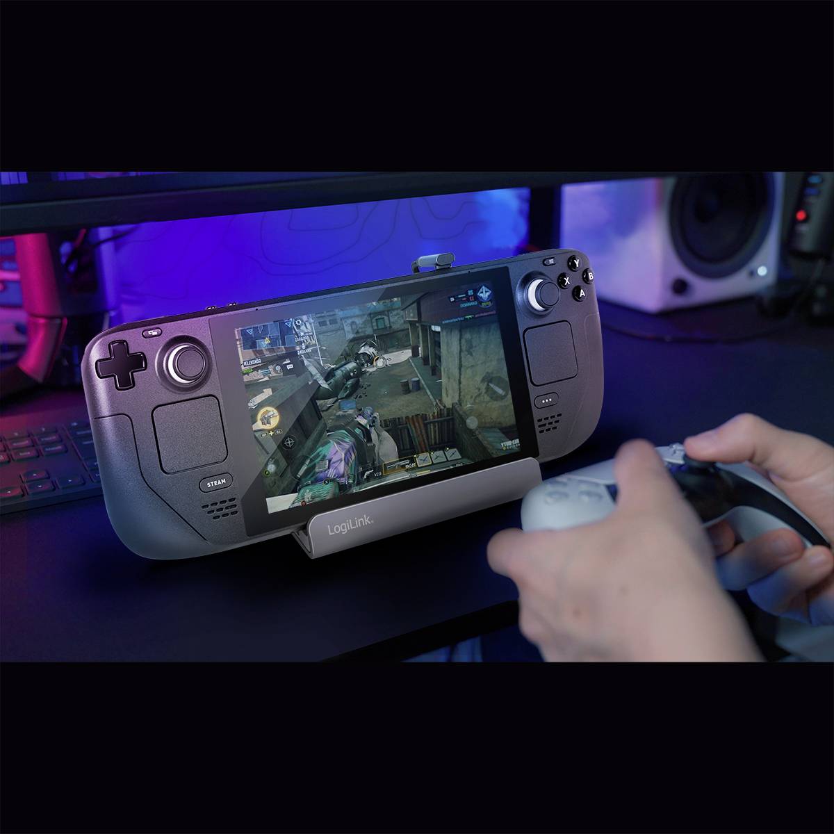 Eine Person spielt ein Videospiel auf einem tragbaren Spielegerät mit Bildschirm. Links sind Lautsprecher erkennbar.