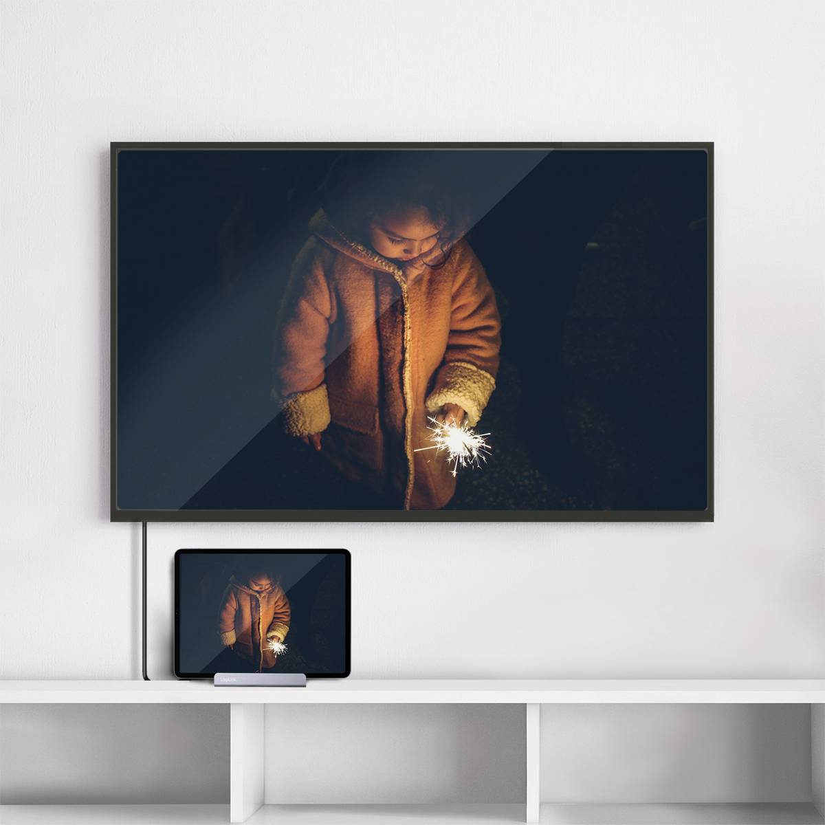 Ein Kind in einem Wintermantel steht im Dunkeln und hält eine leuchtende Wunderkerze. Das Bild ist auf einem Fernseher und einem Tablet zu sehen.