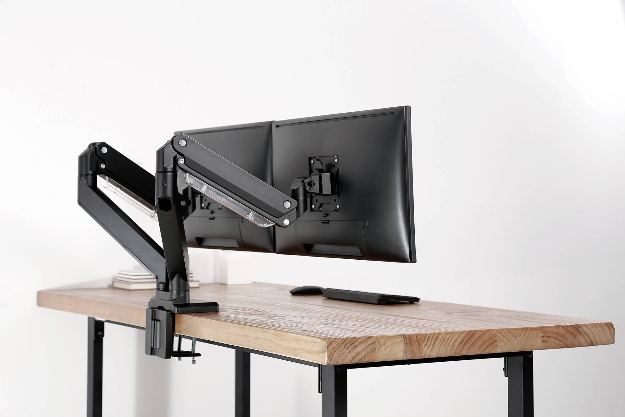 Ein Schreibtisch mit zwei Monitoren an verstellbaren Halterungen, zeigt eine moderne Büroeinrichtung.