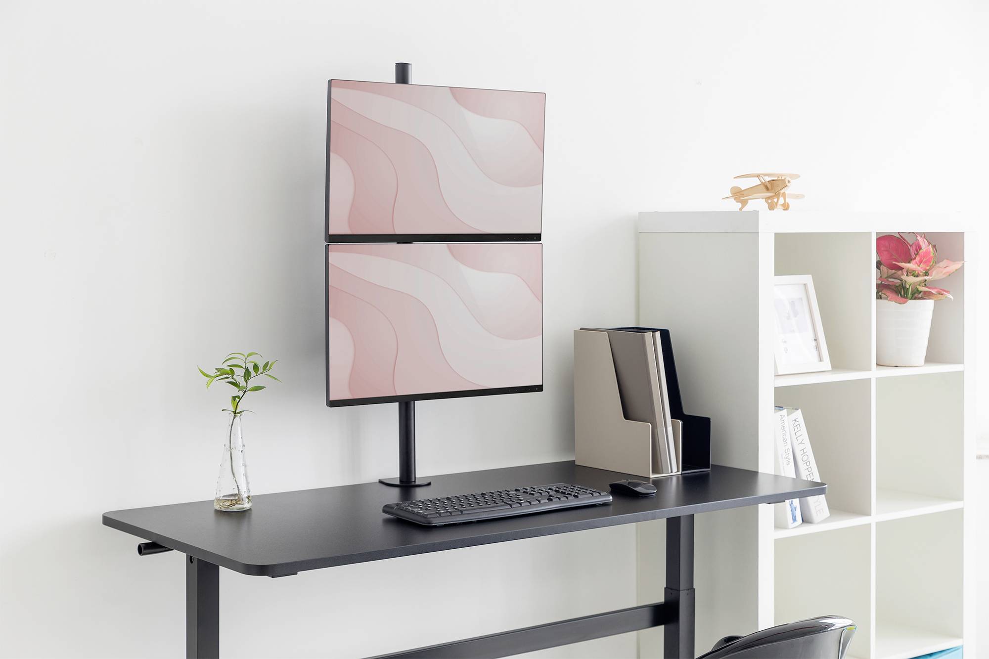 Ein moderner, schwarzer Stehschreibtisch mit zwei übereinander platzierten Monitoren. Links eine kleine Pflanze, rechts ein Regal.