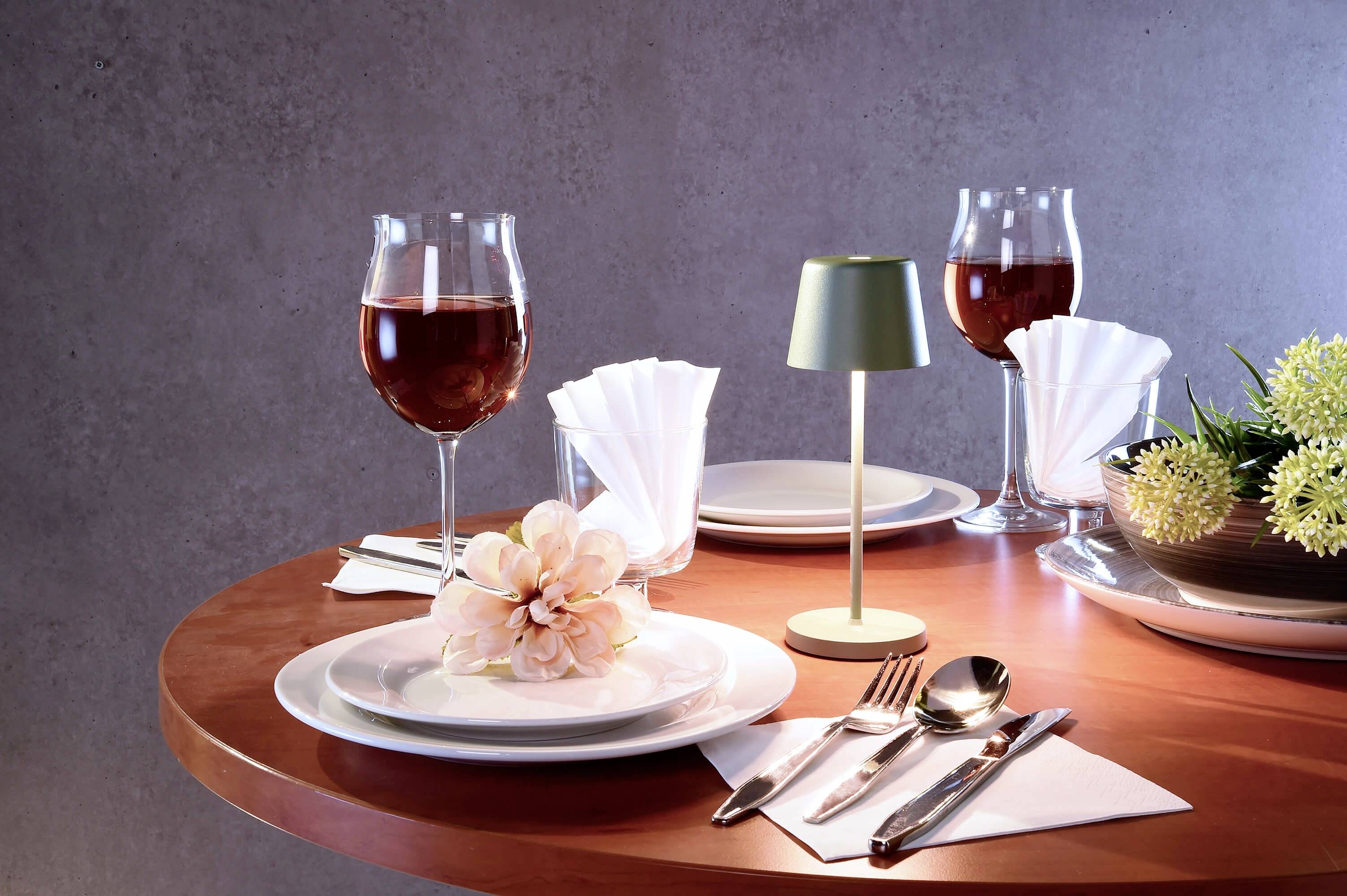 Ein elegant gedeckter Tisch mit Weingläsern, Blumen, Tellern und Besteck. Eine kleine Lampe steht in der Mitte.