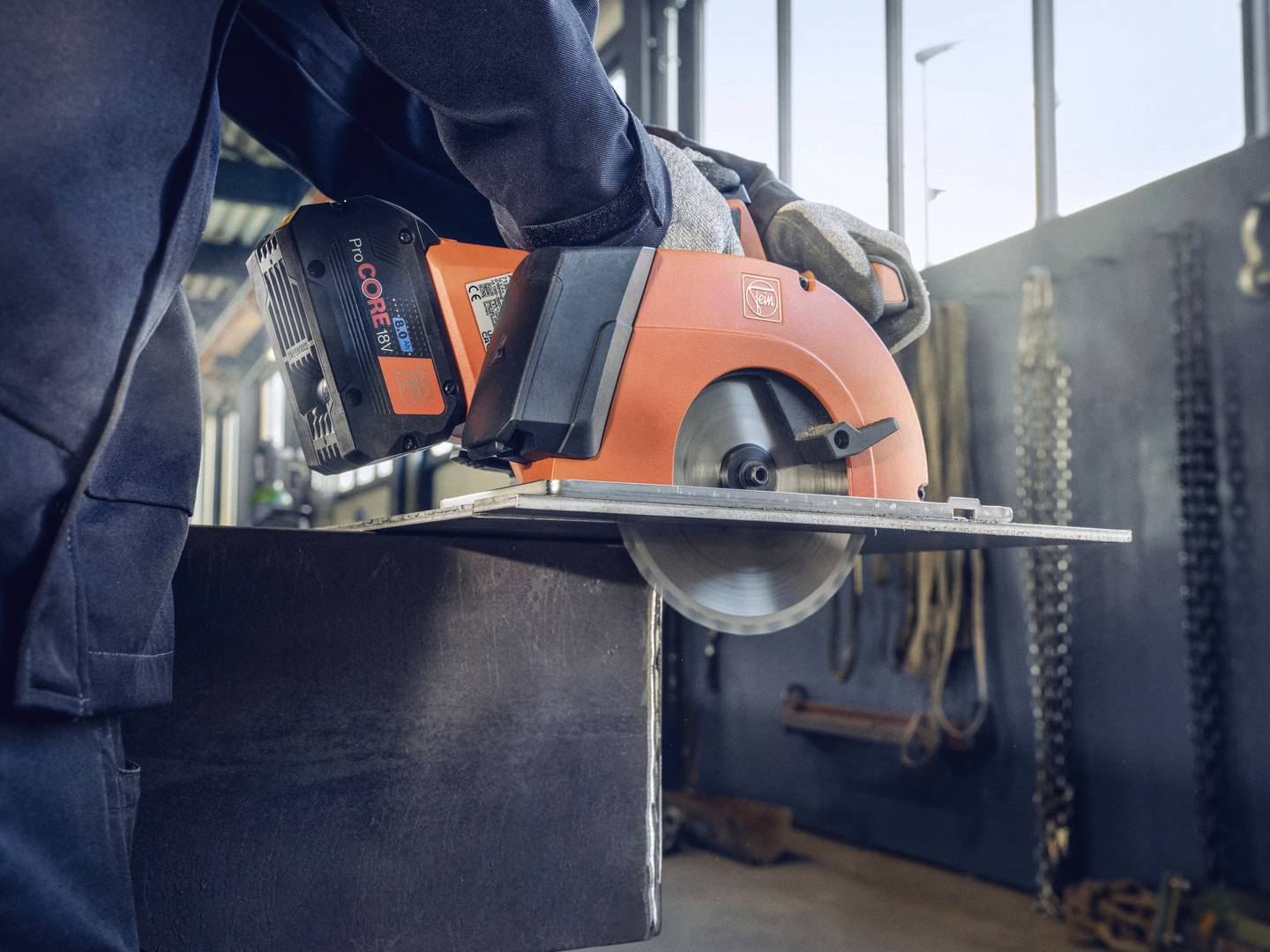 Eine Person verwendet eine orangefarbene Handkreissäge, um ein Metallstück in einer Werkstatt zu schneiden. Werkzeuge sind im Hintergrund sichtbar.