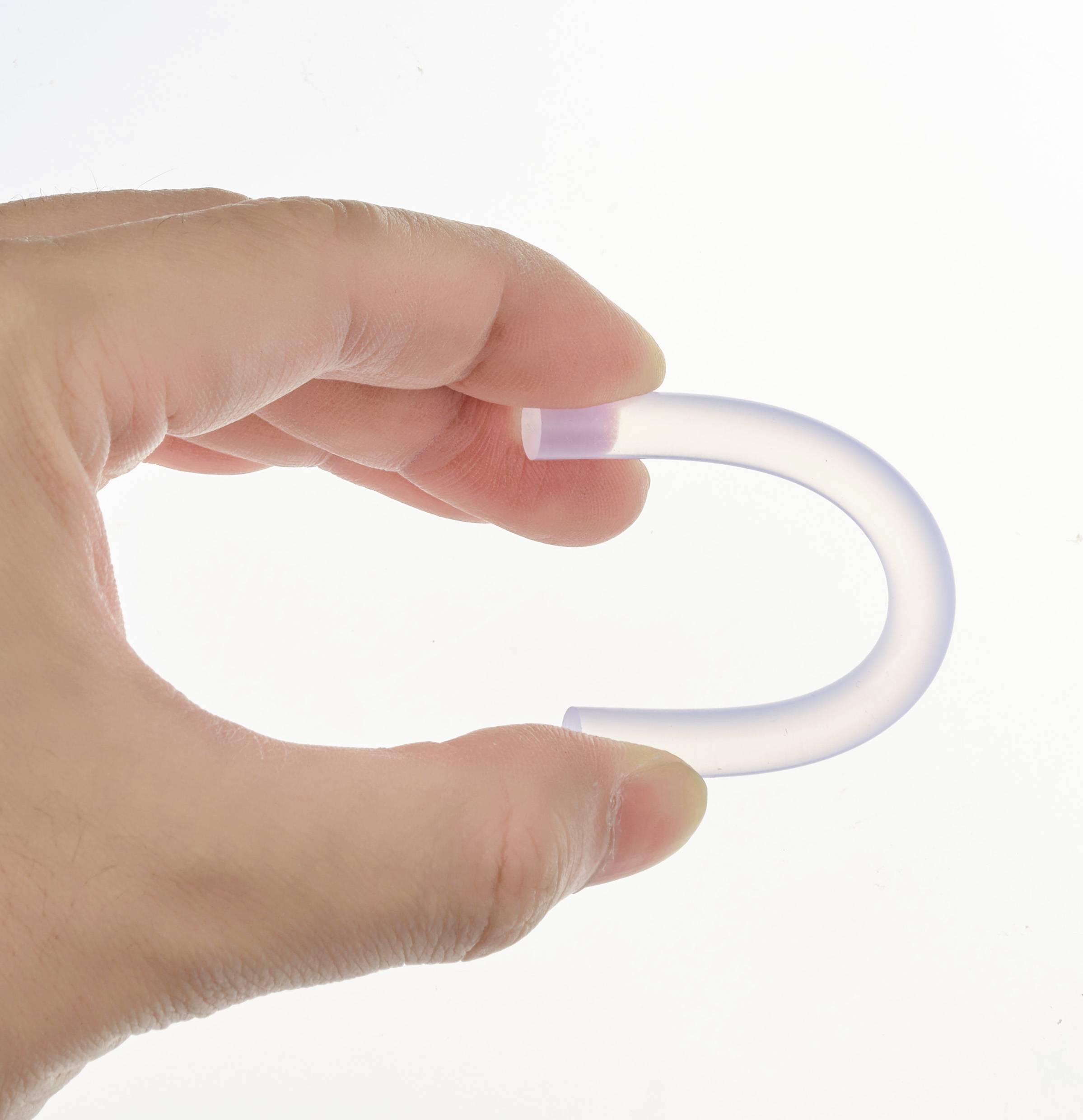 Eine Hand hält ein transparentes, gebogenes Objekt, das wie ein kleines U aussieht. Das Licht scheint leicht durch das Material.