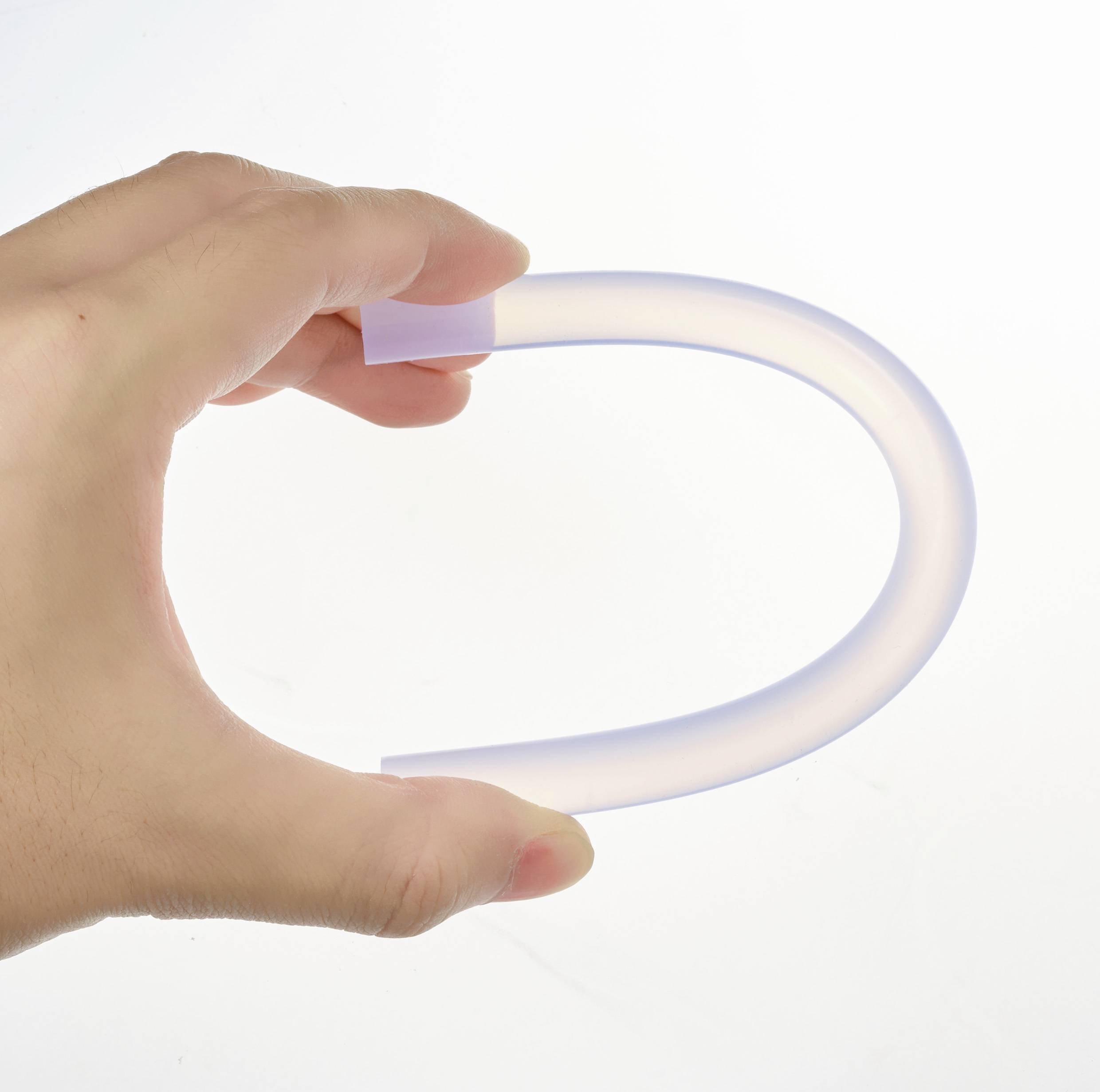 Eine menschliche Hand hält einen transparenten, flexiblen Schlauch in einer gebogenen Form vor einem neutralen Hintergrund.