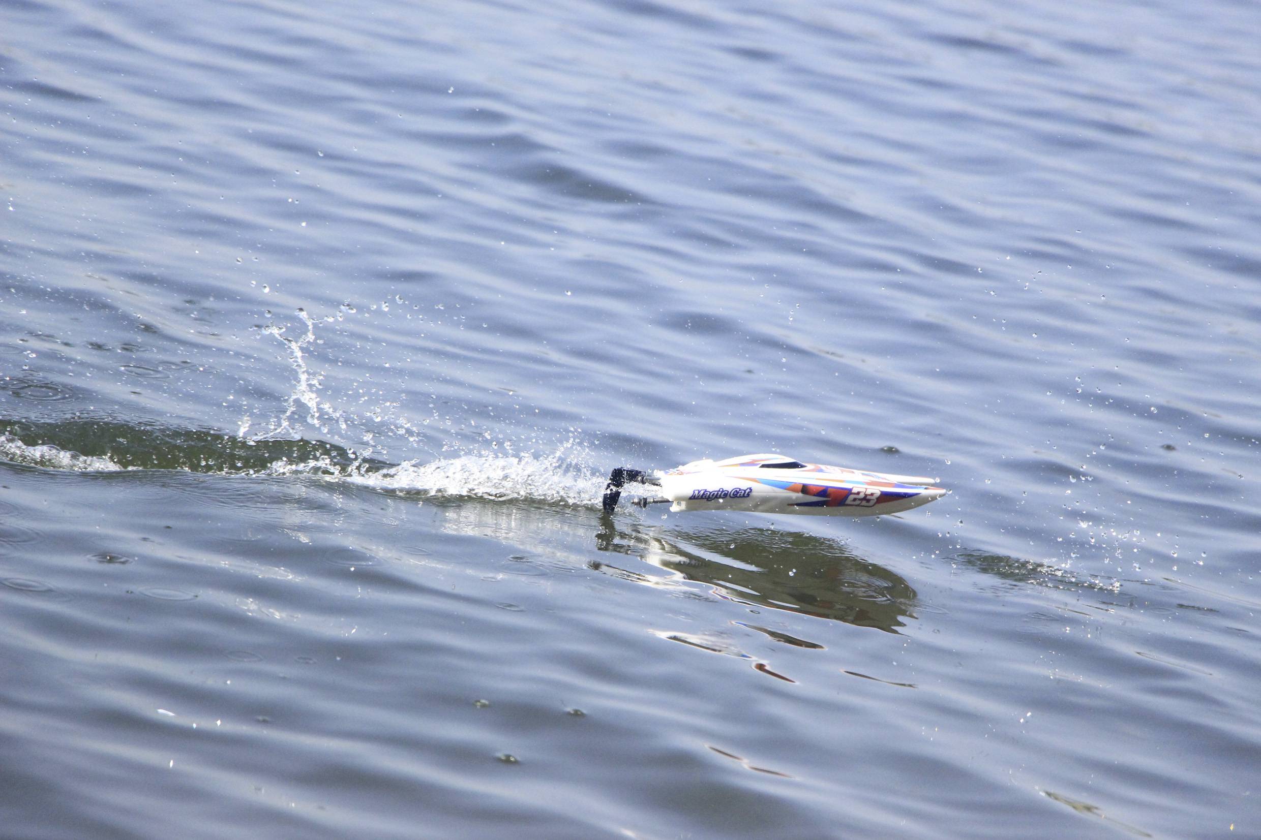 Ein kleines Modellboot gleitet schnell über die Wasseroberfläche, zieht Wellen hinter sich her und erzeugt spritzendes Wasser.