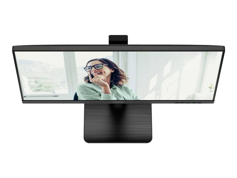 Eine lächelnde Person mit Brille sitzt vor einem Monitor in einem hellen Raum. Der Monitor ist zentral im Bild platziert.