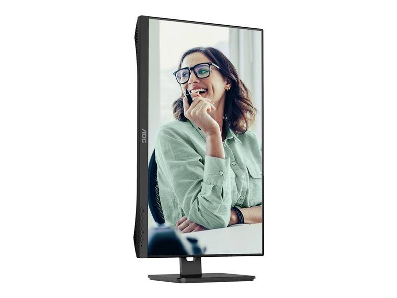 Eine lächelnde Person mit Brille sitzt an einem Monitor, trägt ein grünes Hemd und schaut seitlich in die Ferne.