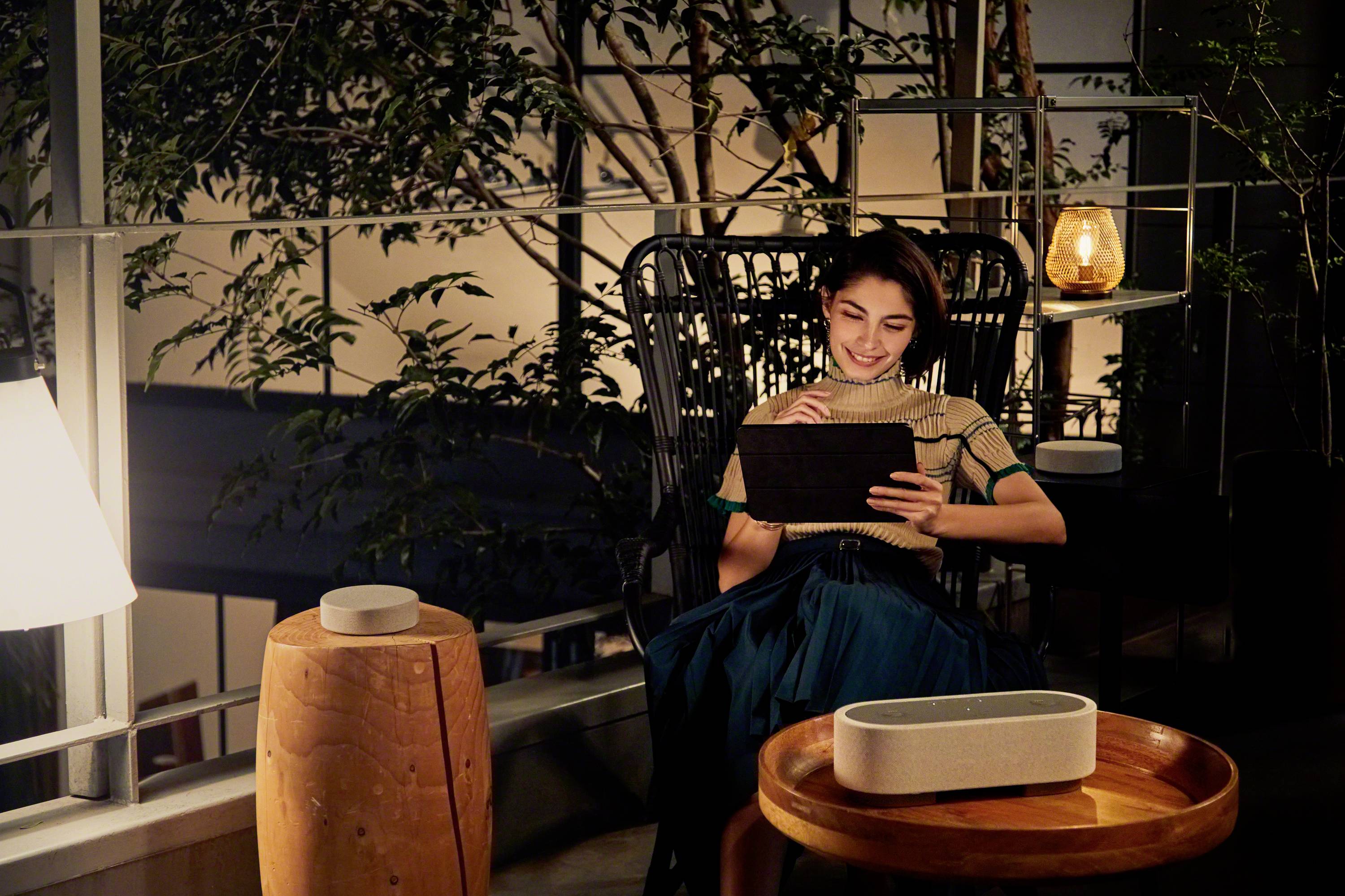 Eine Person sitzt abends auf einem Balkon, liest auf einem Tablet, umgeben von Pflanzen und sanfter Beleuchtung.