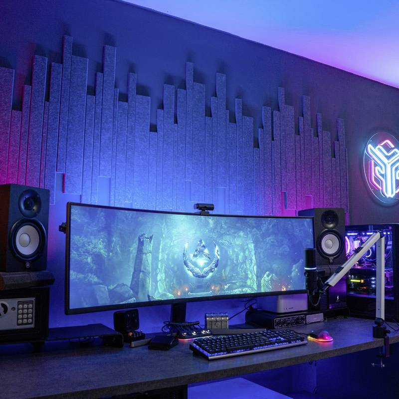 Gaming-Setup mit beleuchtetem, gebogenem Monitor, umgeben von zwei Lautsprechern und einem leuchtenden Computergehäuse auf einem Tisch.