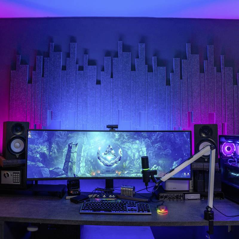 Eine Arbeitsstation mit einem ultrabreiten Monitor, umgeben von Lautsprechern und RGB-Beleuchtung, vermutlich für Multimedia-Nutzung.