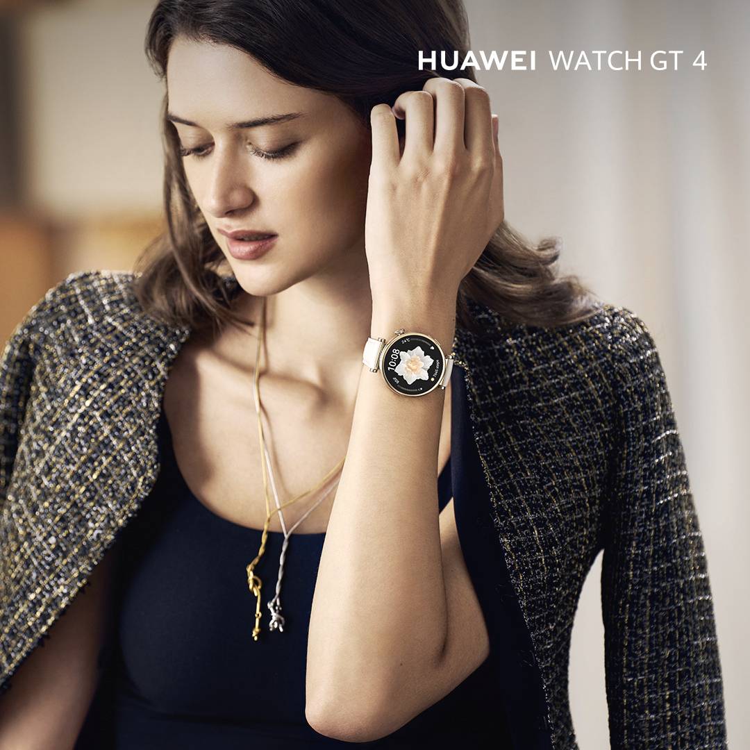 Eine Frau trägt die 'Huawei Watch GT 4', ein eleganter Chronograph im luxuriösen Stil. Sie ist schick gekleidet in einem sakkoartigen Oberteil.