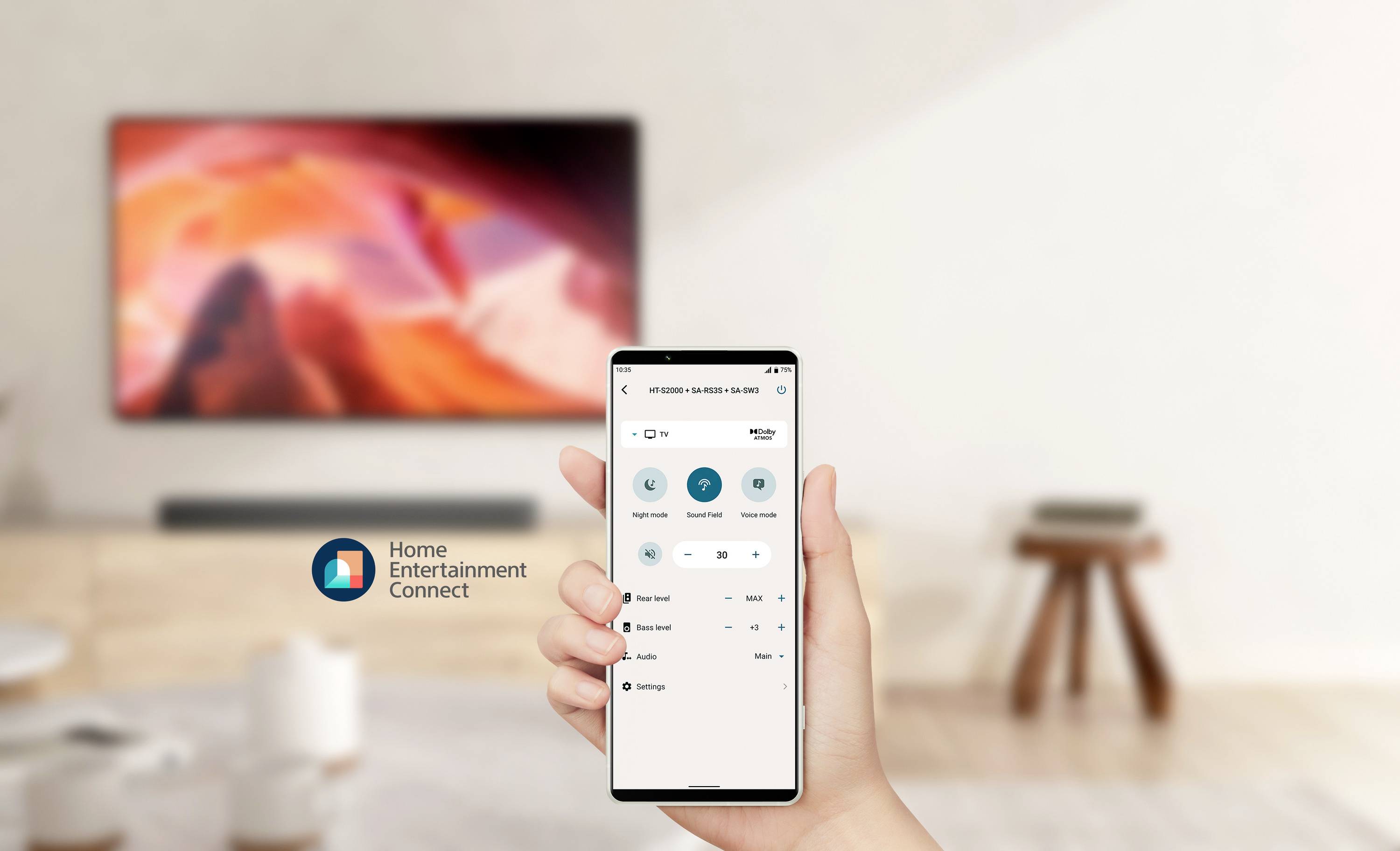 Ein Smartphone zeigt die App 'Home Entertainment Connect' zur Steuerung eines Fernsehers. Im Hintergrund unscharf ein eingeschalteter Fernseher.