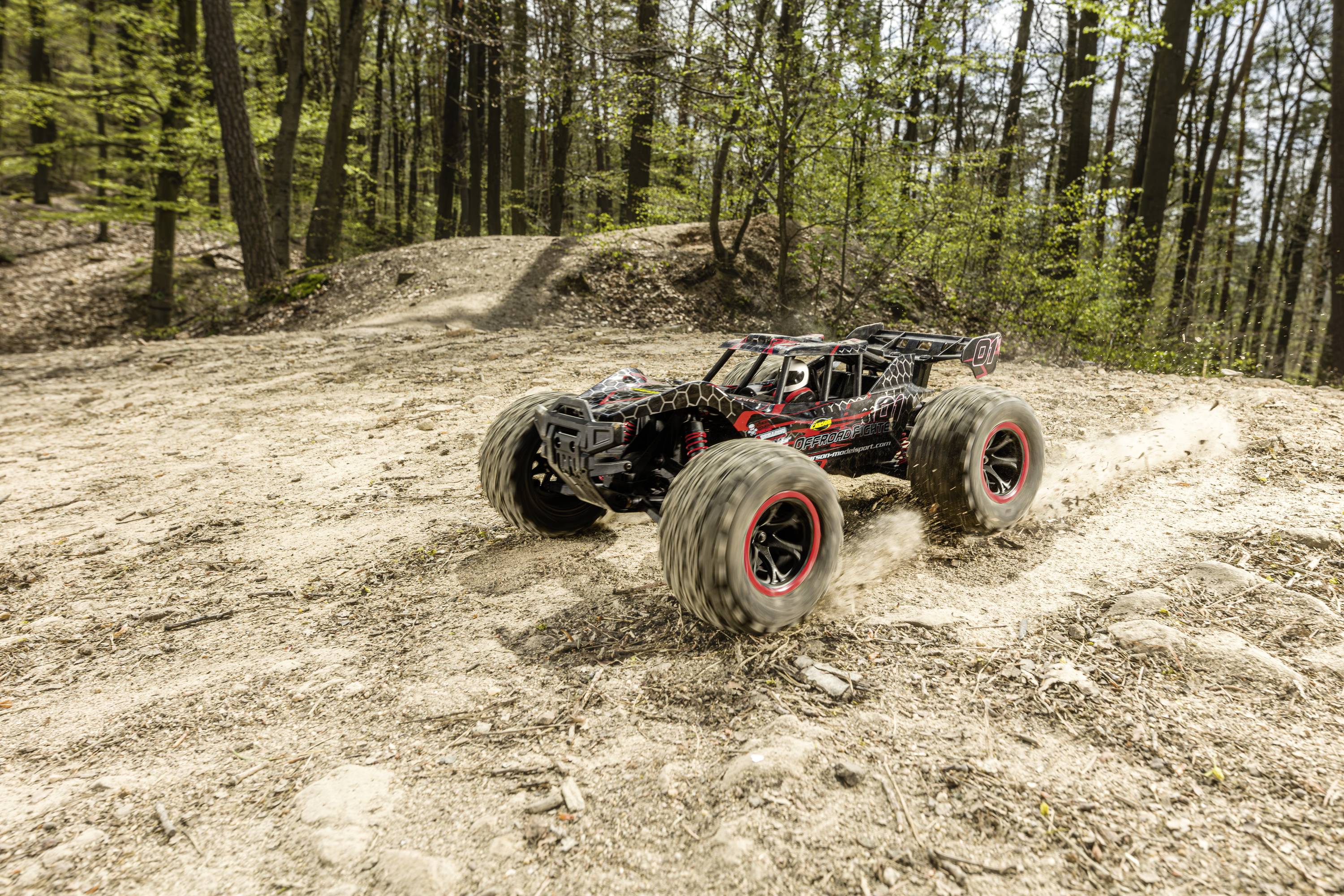 Ein ferngesteuertes Auto fährt mit hoher Geschwindigkeit über einen unebenen Waldweg, wobei Staub von den Rädern aufgewirbelt wird.