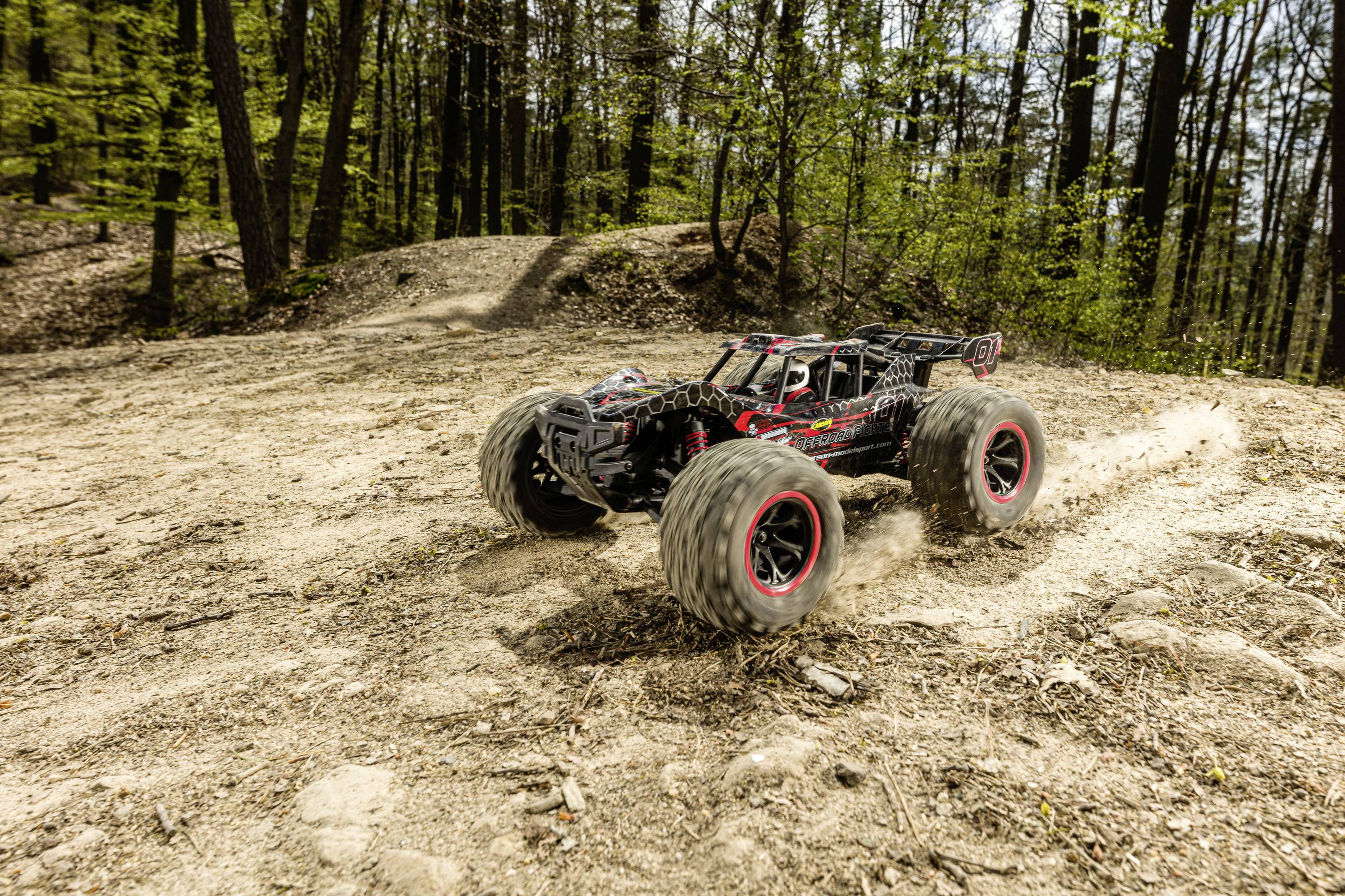 Ein ferngesteuertes Auto fährt schnell über einen sandigen Waldweg. Große Reifen wirbeln Staub auf, während das Auto um eine Kurve driftet.
