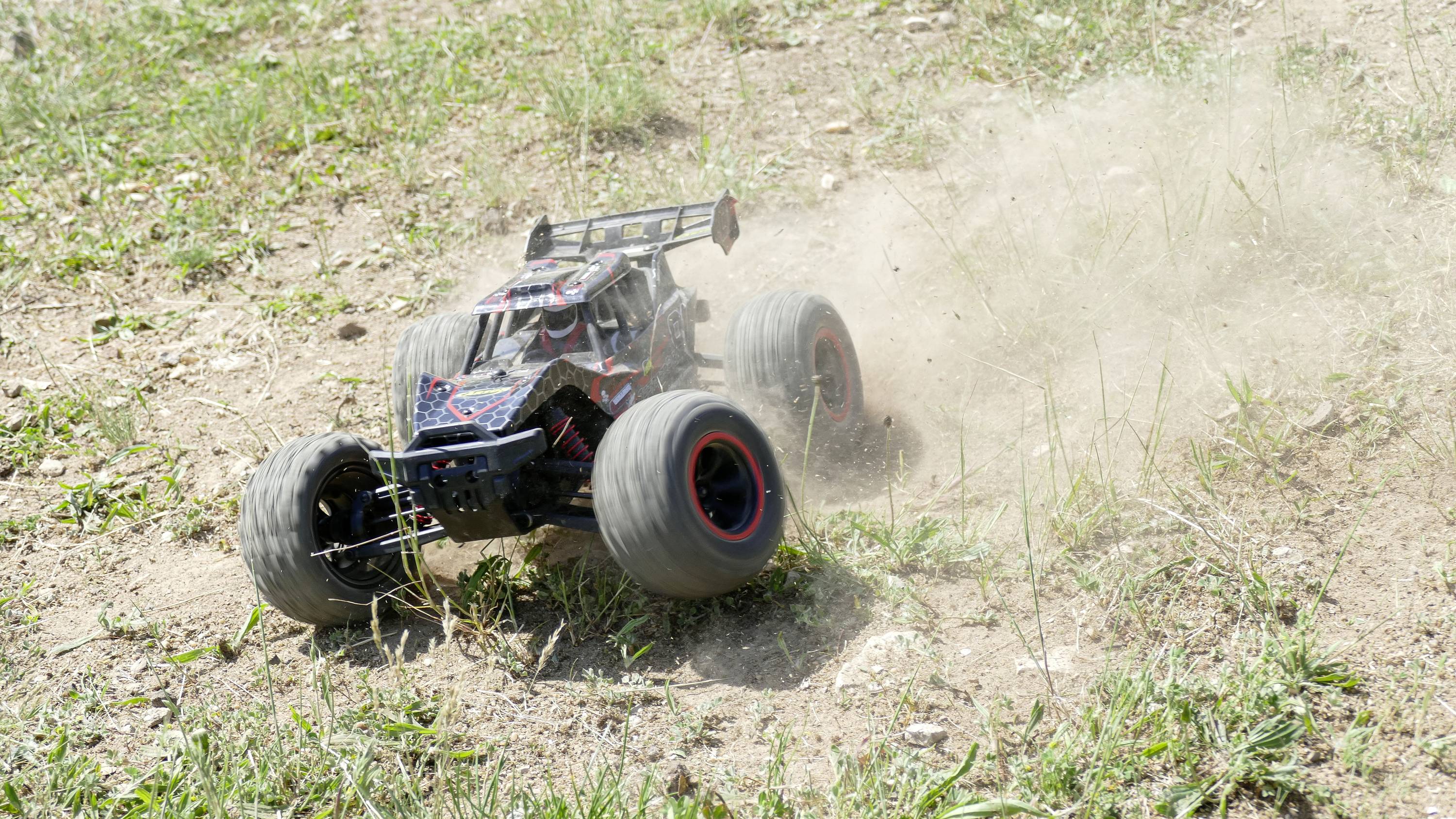 Ein ferngesteuertes Auto fährt schnell über eine staubige, grasbewachsene Fläche und wirbelt dabei Schmutz und Staub auf.