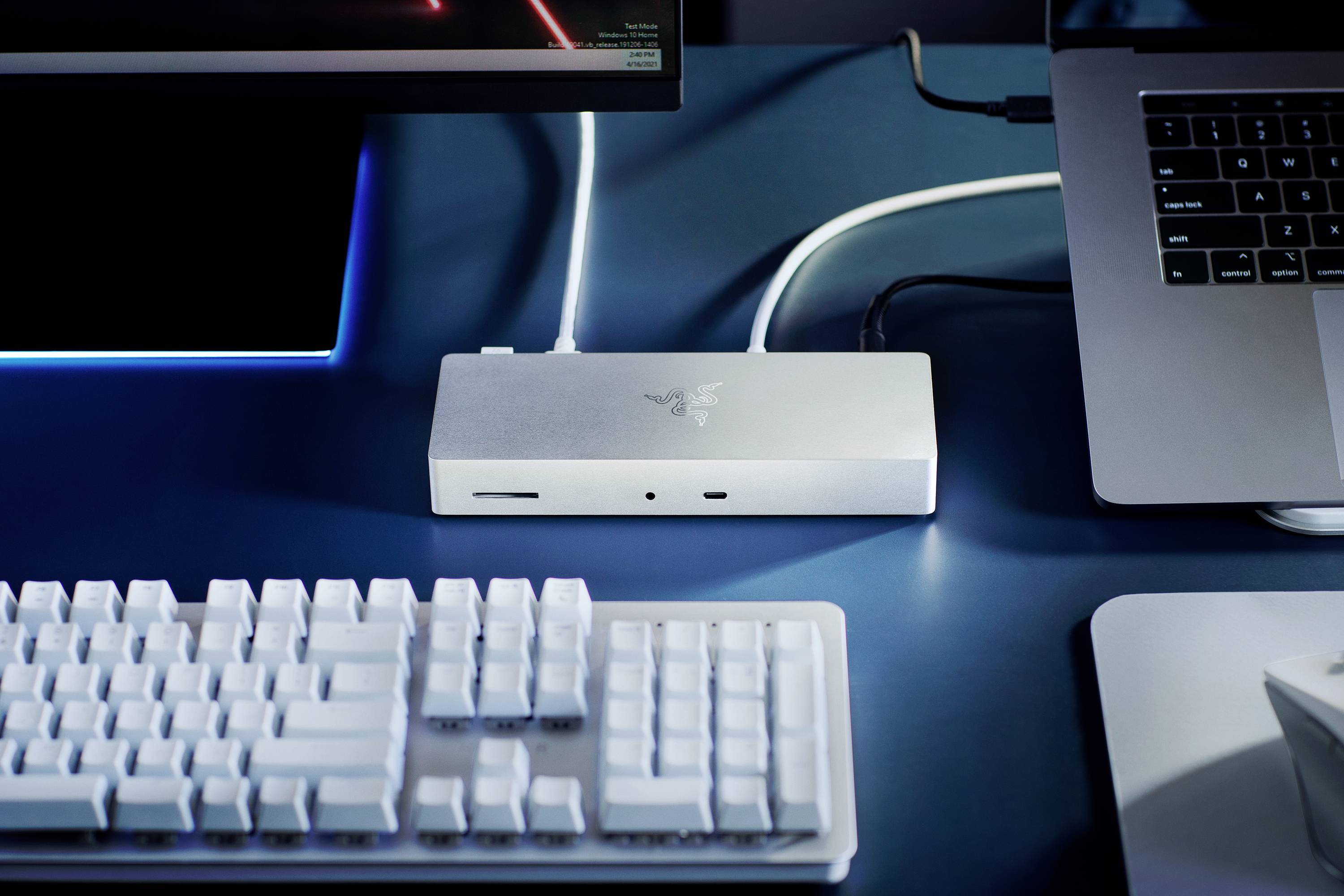 Ein silbernes Dock verbindet einen Laptop mit einem externen Monitor und einer Tastatur auf einem Schreibtisch.