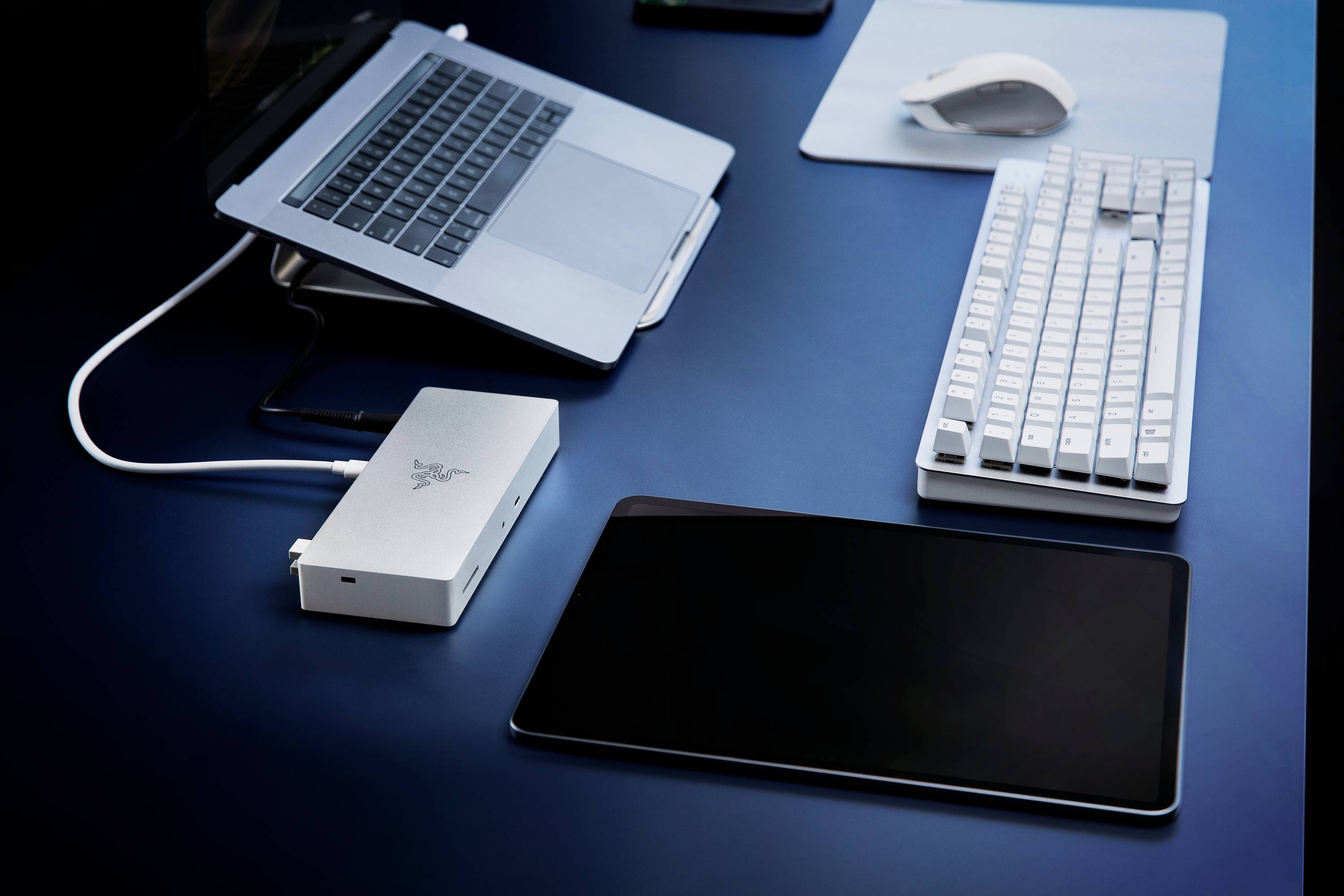Ein Laptop, eine externe Festplatte, eine Tastatur, eine Maus und ein Tablet liegen auf einem blauen Tisch, verbunden für die Arbeit.