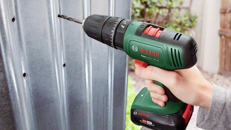 Eine Hand hält einen Akku-Bohrschrauber der Marke Bosch und bohrt ein Loch in ein Metallblech. Die Umgebung ist unscharf.