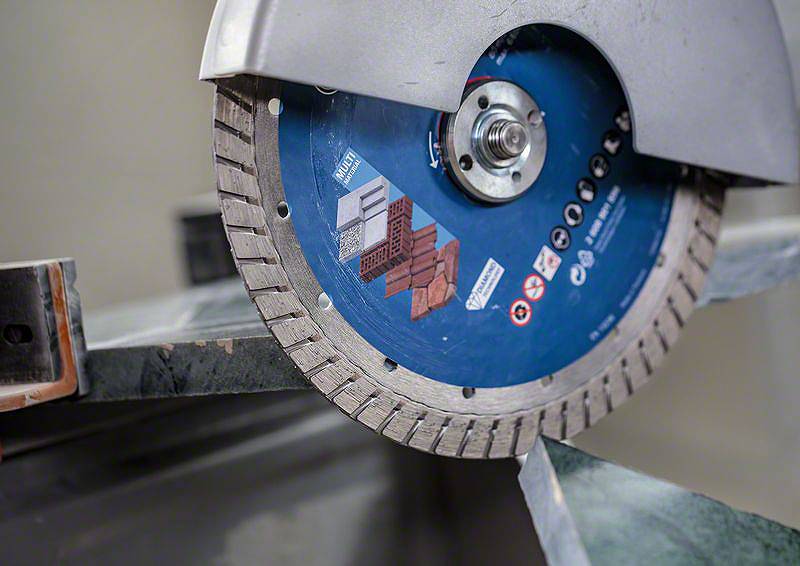 Ein Metallschneideblatt wird in einer Maschine montiert. Das Blatt ist blau und mit Symbolen für verschiedene Materialien gekennzeichnet.