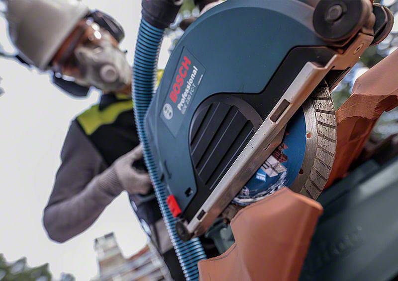 Eine Person mit Schutzbrille und Atemmaske arbeitet mit einer elektrischen Säge an einem orangefarbenen Material im Freien.