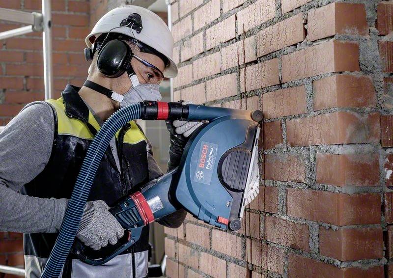Arbeiter mit Schutzbrille, Helm und Maske schneidet Ziegelwand mit einer elektrischen Fräse.
