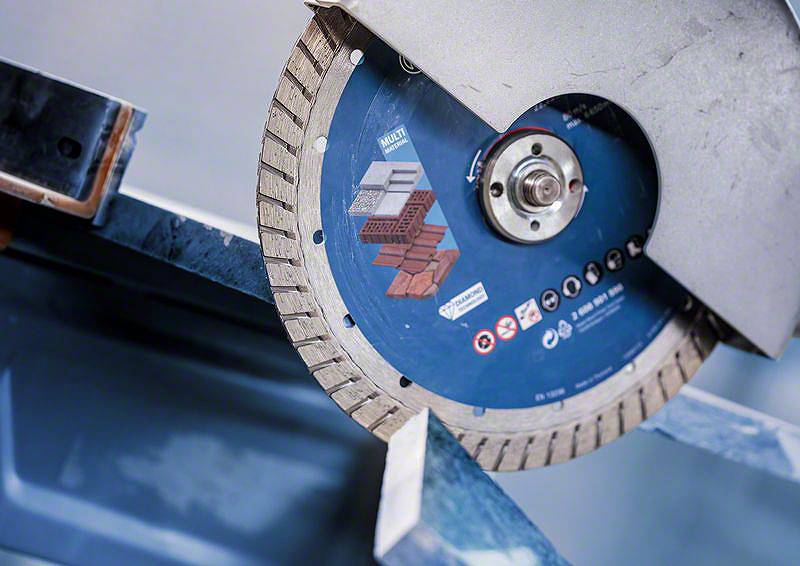 Nahaufnahme einer Kreissäge mit diamantbeschichteter Klinge, die auf eine Metallstange gerichtet ist. Die Klinge ist blau und wird für das Schneiden von Baumaterialien verwendet.