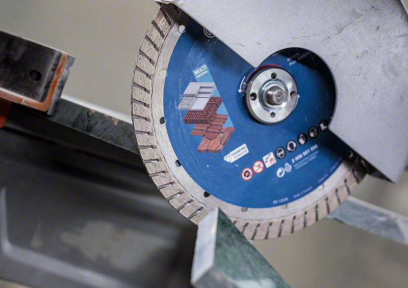 Kreissägeblatt schneidet durch Metallstück; blaues Sägeblatt mit Abbildungen von Beton und Ziegeln, zeigt Materialvielfalt.