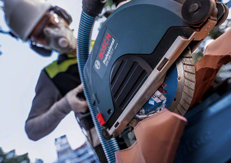 Eine Person mit Schutzbrille und Atemmaske schneidet ein Ziegeldach mit einer elektrischen Säge. Markenname 'Bosch' auf der Säge sichtbar.