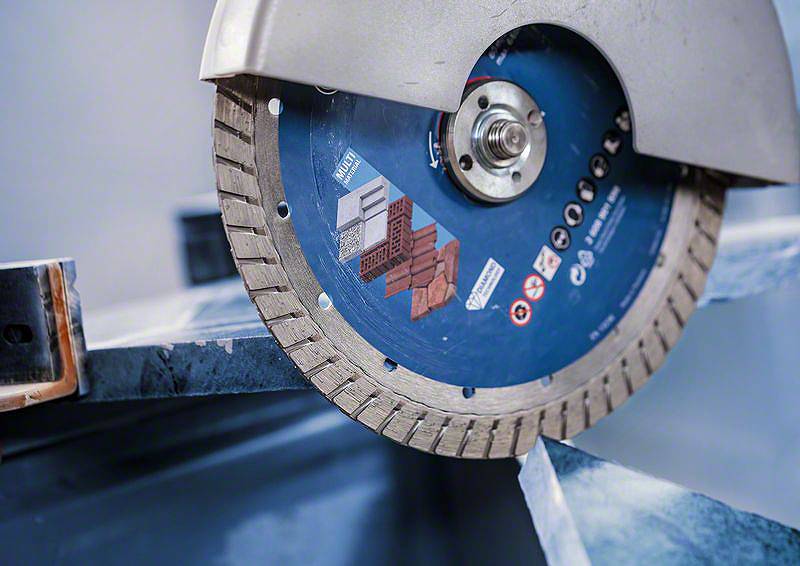 Eine Kreissäge mit diamantbeschichtetem Sägeblatt schneidet einen metallischen Gegenstand. Sicherheitssymbole sind auf dem Blatt sichtbar.