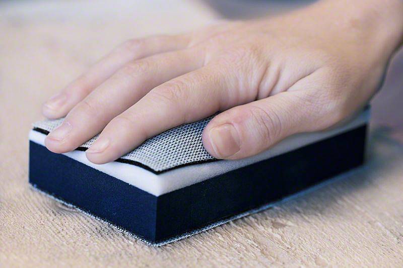 Eine Hand, die einen Schleifblock über eine Holzoberfläche führt, um diese zu glätten.