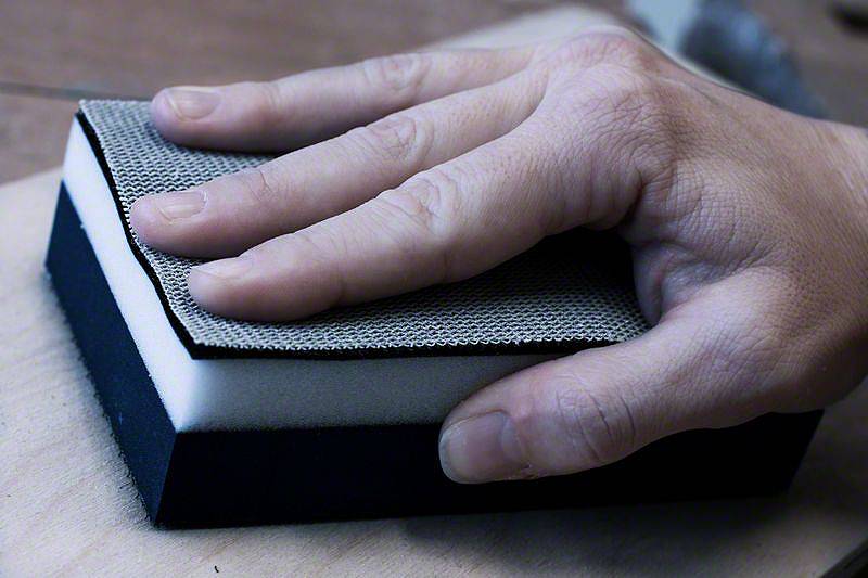 Eine Hand hält einen Schleifblock und schleift eine Holzoberfläche.