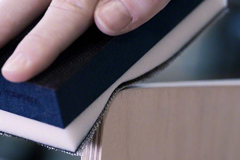 Eine Hand schleift mit einem Schleifschwamm eine Holzkante, um die Oberfläche zu glätten.