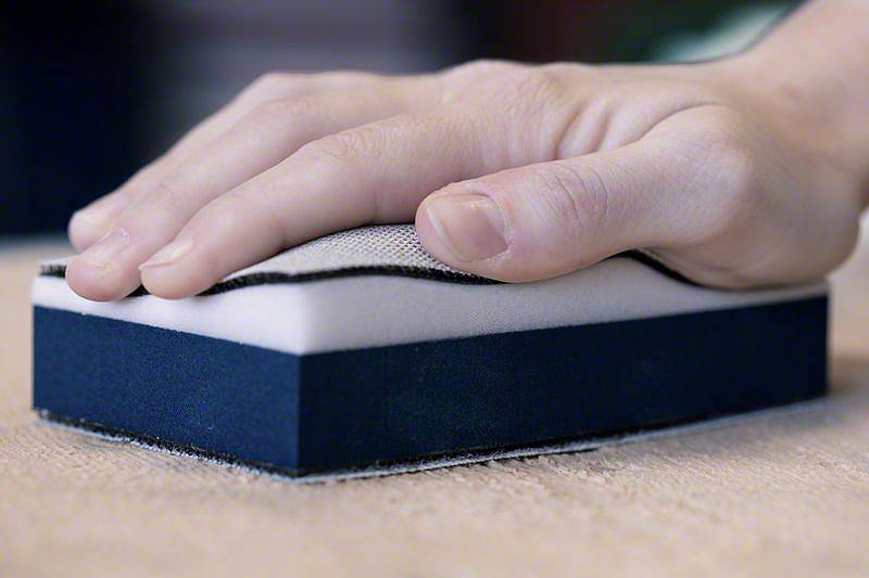 Eine Hand schleift mit einem Schleifblock eine Holzoberfläche.