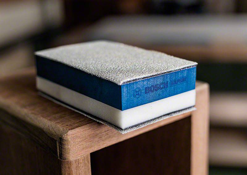 Blauer Bosch-Schleifschwamm liegt auf einer Holzkante. Ideal für präzises Schleifen in Ecken und schwer erreichbaren Stellen.