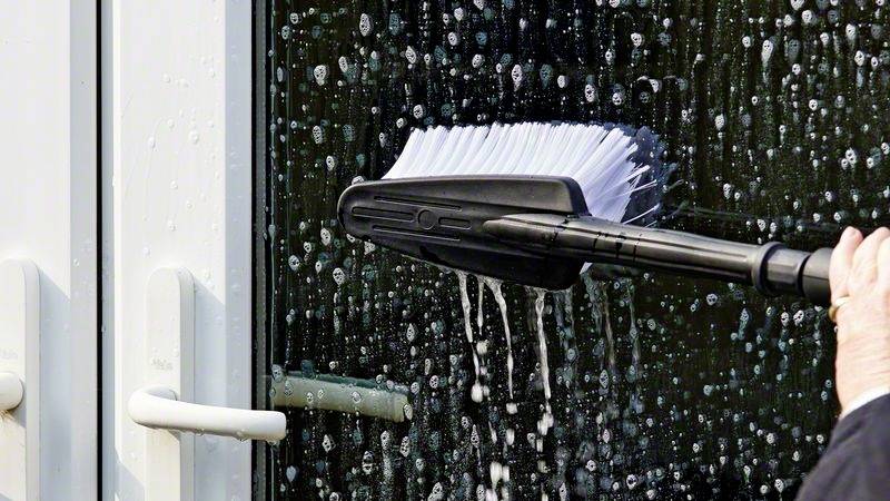 Eine Person reinigt mit einer Bürste ein verspiegeltes Glasfenster, auf dem Seifenlauge zu sehen ist.