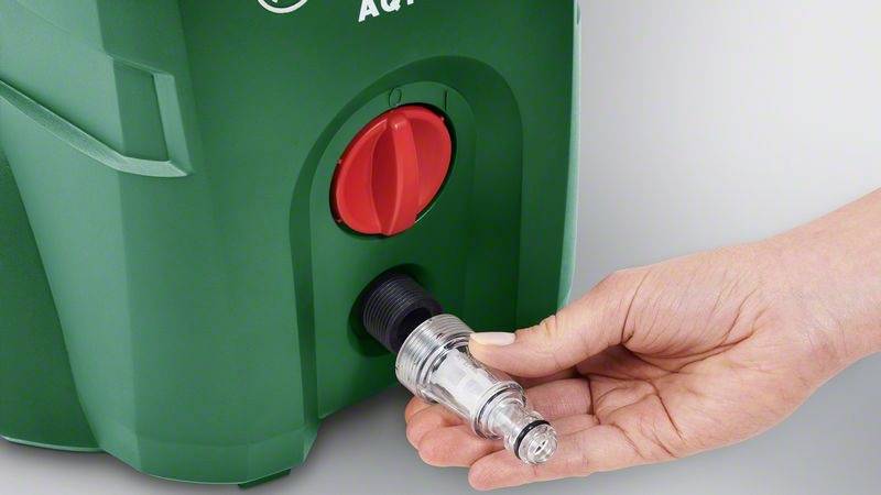 Eine Hand hält ein durchsichtiges Ventil vor einem grünen Gerät mit rotem Drehknopf; zeigt Anschlussvorbereitung.