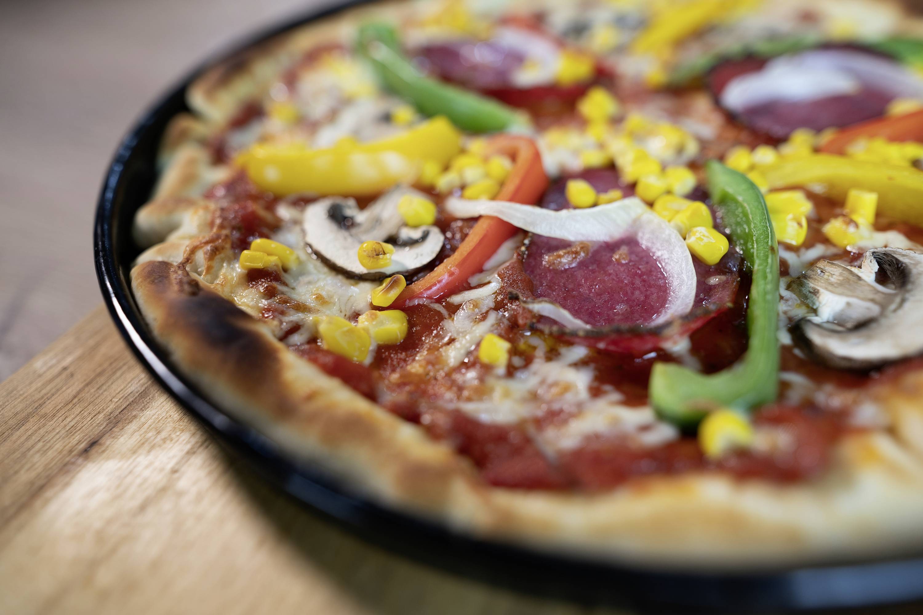 Pizza mit Salami, Paprika, Mais und Champignons auf einem Holzbrett.