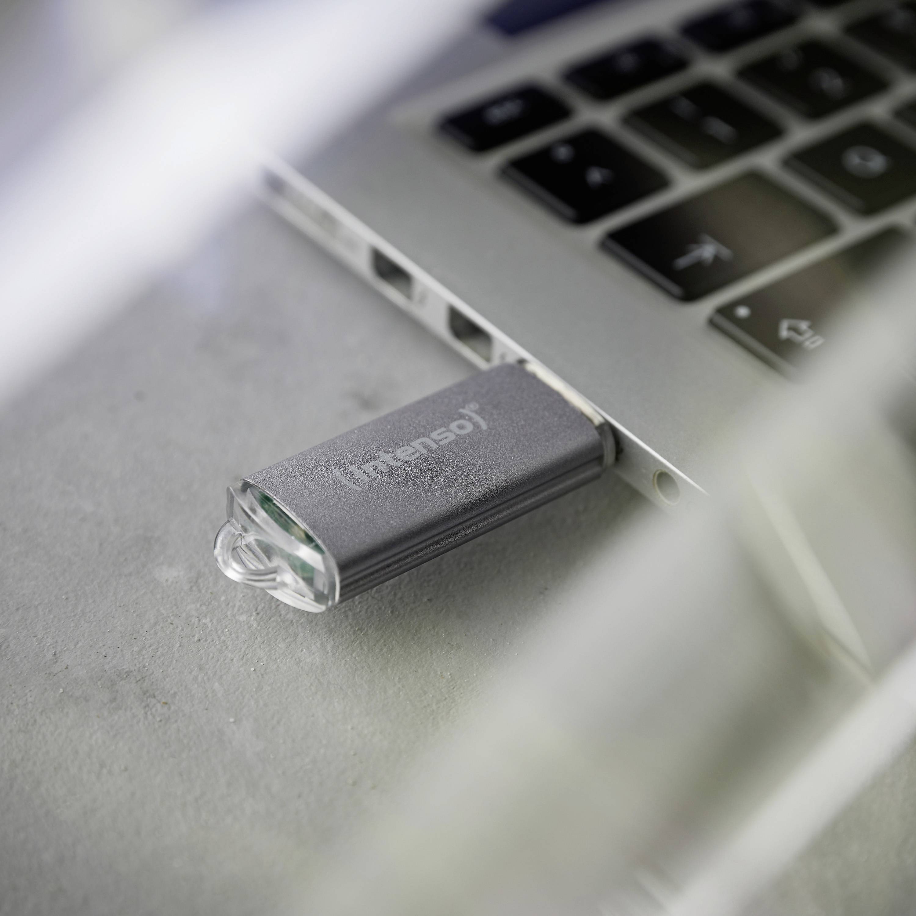 USB-Stick der Marke Intenso, eingesteckt in einen Laptop auf einem grauen Tisch. Der Laptop ist teilweise sichtbar.