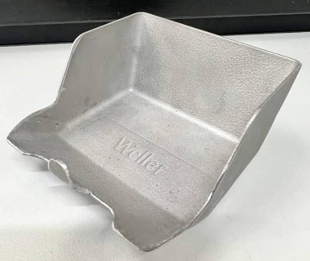 Ein silbernes Metallbehältnis mit der Aufschrift 'Weller' auf dem Boden. Es hat abgerundete Kanten und eine raue Oberfläche.