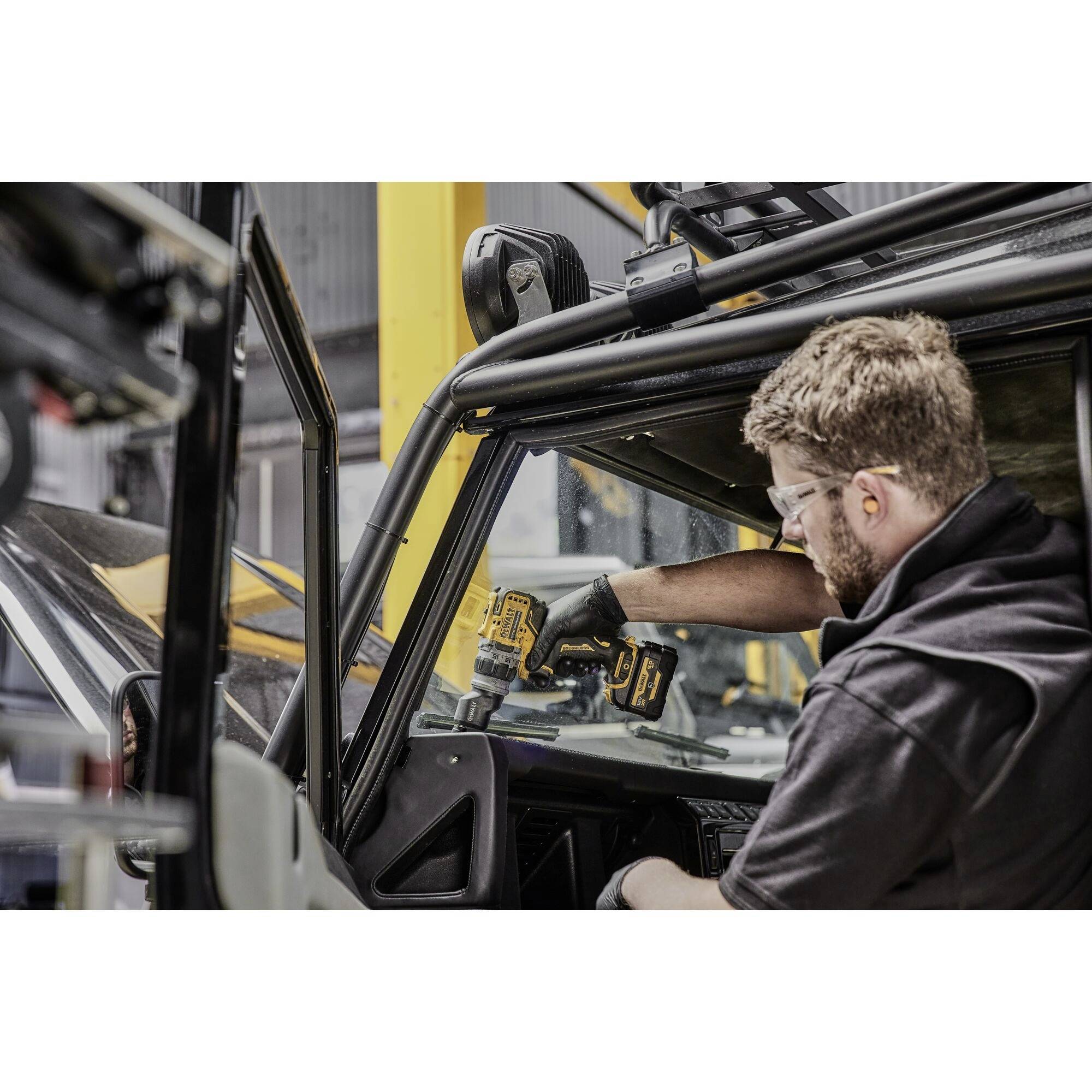 Eine Person in Schutzbrille und Handschuhen arbeitet an einem Fahrzeug mit einem Elektrowerkzeug. Sie befestigt oder repariert Teile.