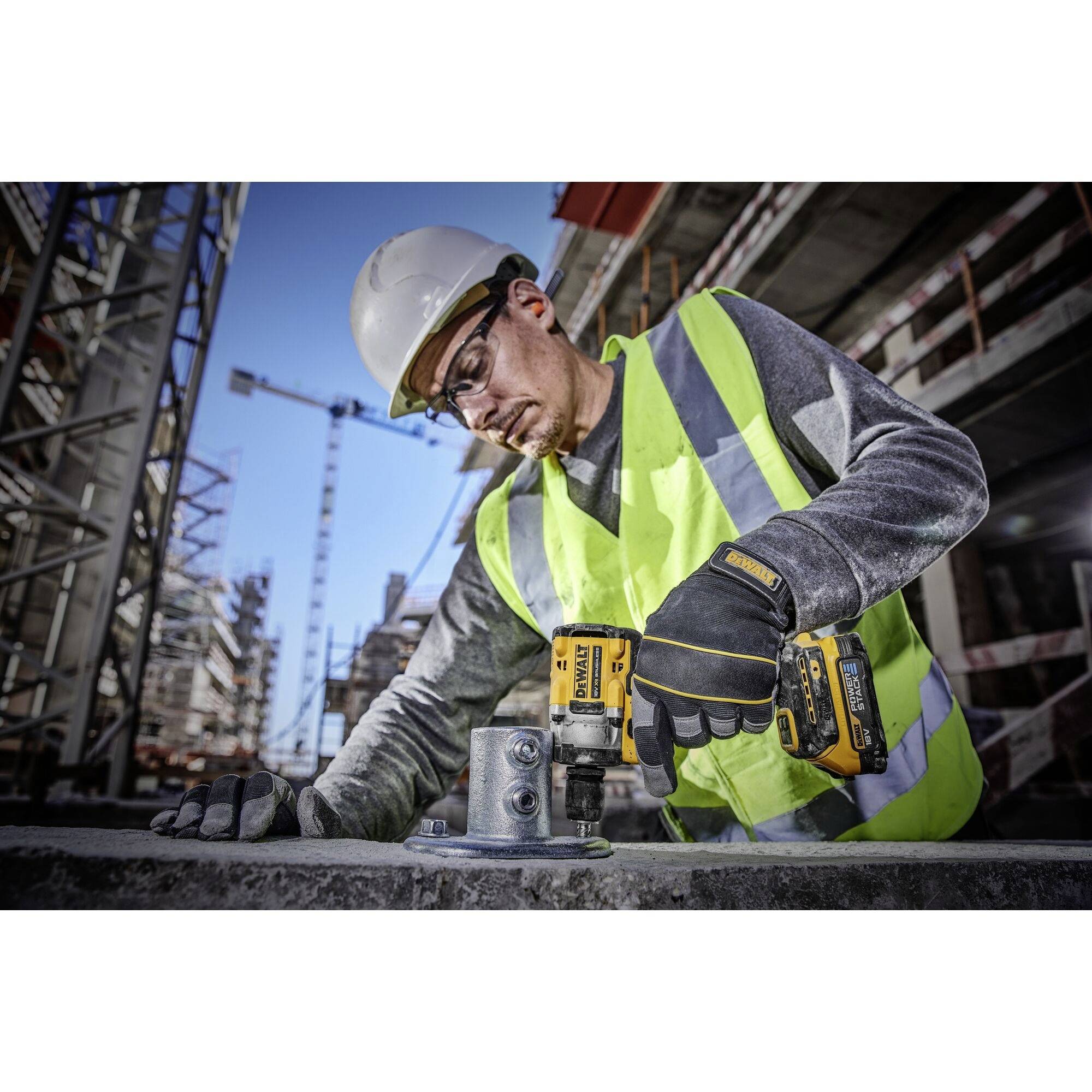 Ein Bauarbeiter in Schutzkleidung verwendet eine Bohrmaschine, um eine Metallplatte auf einer Baustelle zu befestigen. Hintergrund zeigt Baugerüste.