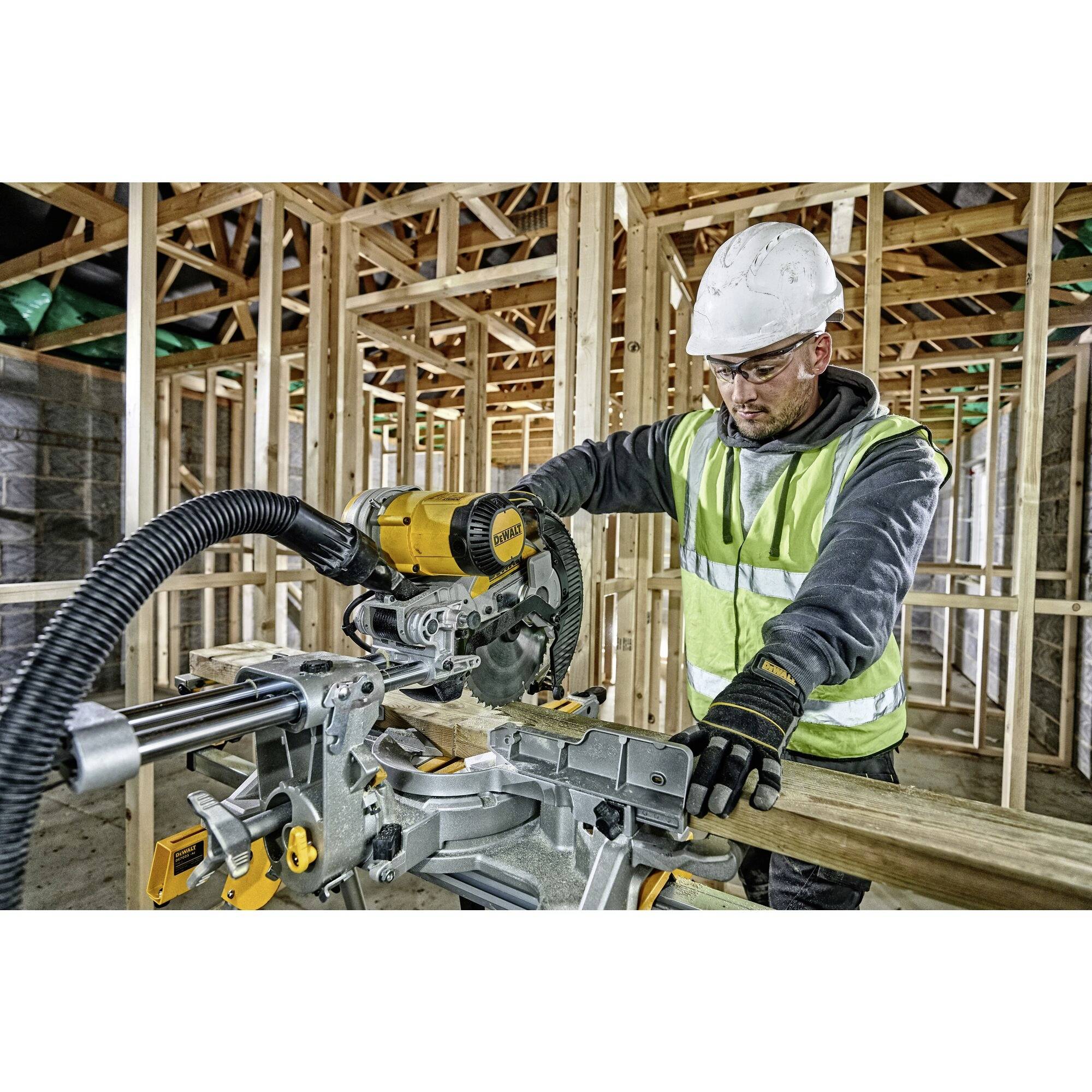 Ein Bauarbeiter mit Schutzhelm und Sicherheitsweste benutzt eine elektrische Gehrungssäge, um Holz in einem Rohbau zu schneiden.