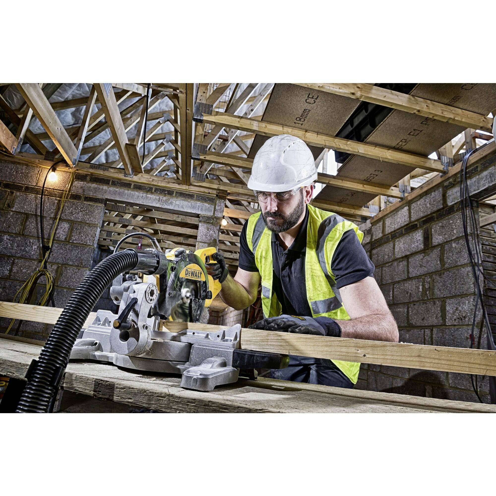 Ein Bauarbeiter mit Schutzhelm und Weste benutzt eine Kreissäge, um Holz in einem teils errichteten Gebäude mit Holzgestell zu schneiden.