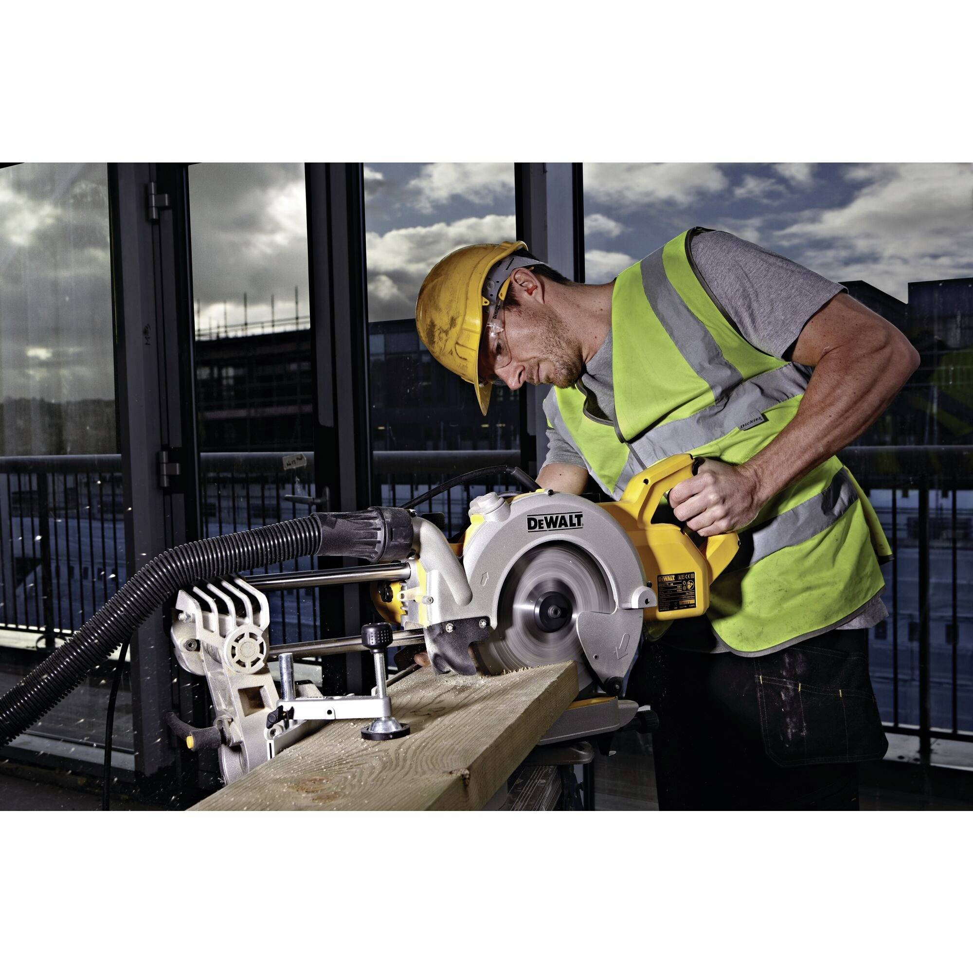 Eine Person mit Schutzhelm und Warnweste schneidet ein Holzbrett mit einer elektrischen Kreissäge in einem Industriegebäude.