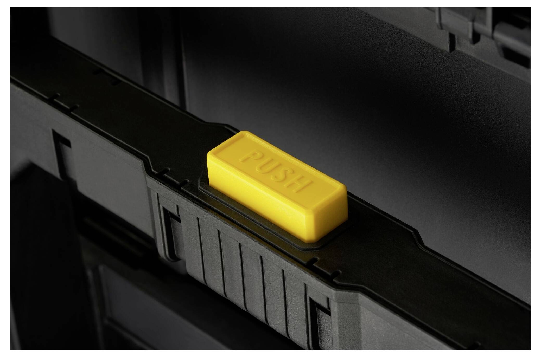 Gelbe 'PUSH'-Taste auf schwarzem Koffer. Die Taste ist zentral platziert und dient zum Öffnen oder Schließen des Koffers.
