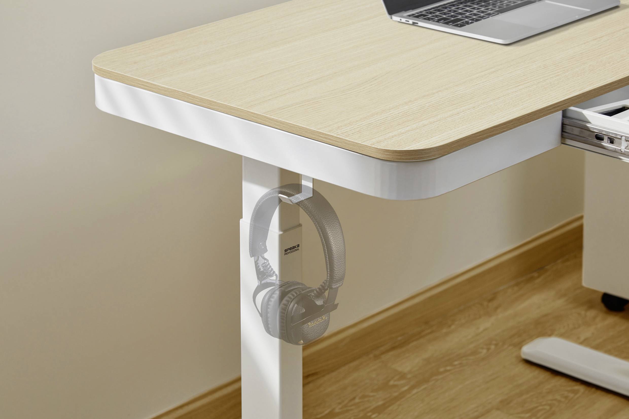 Holztisch mit Laptop, darunter Kopfhörer an einem Haken an der Tischkante aufgehängt.